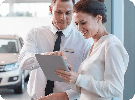 Dos personas mirando un ipadcon un auto de fondo