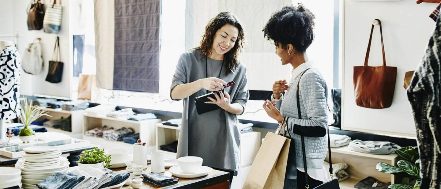 Dos mujeres en una tienda realizando una transacción con su dispositivo móvil