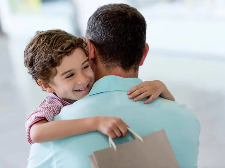 Garantía Diners Club Aadvantage: Un niño en brazos con su bolsa de compra abrazando a su papá