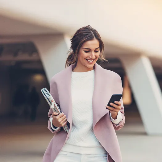 Mujer joven caminando y sonriendo con un teléfono en la mano.