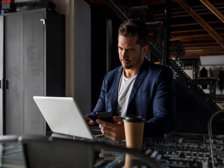 Hombre joven con una computadora y un celular en la mano